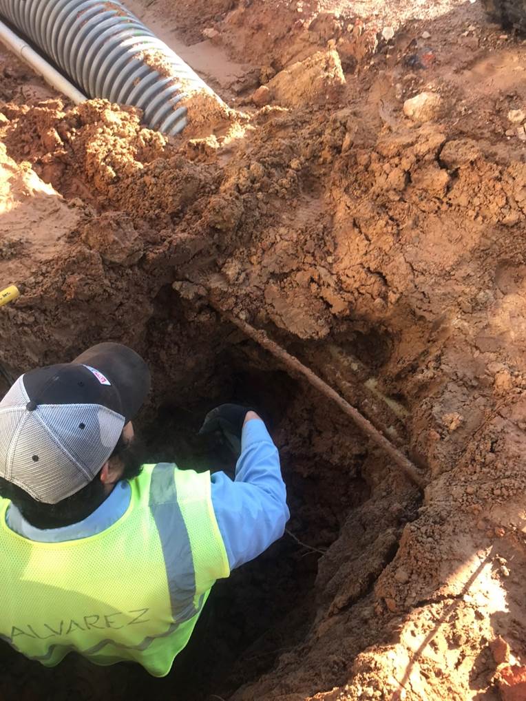A person in a vest and hat working in a hole

Description automatically generated