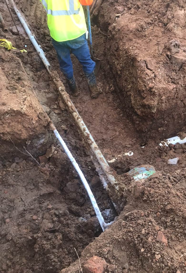 A person in a trench with a pipe

Description automatically generated